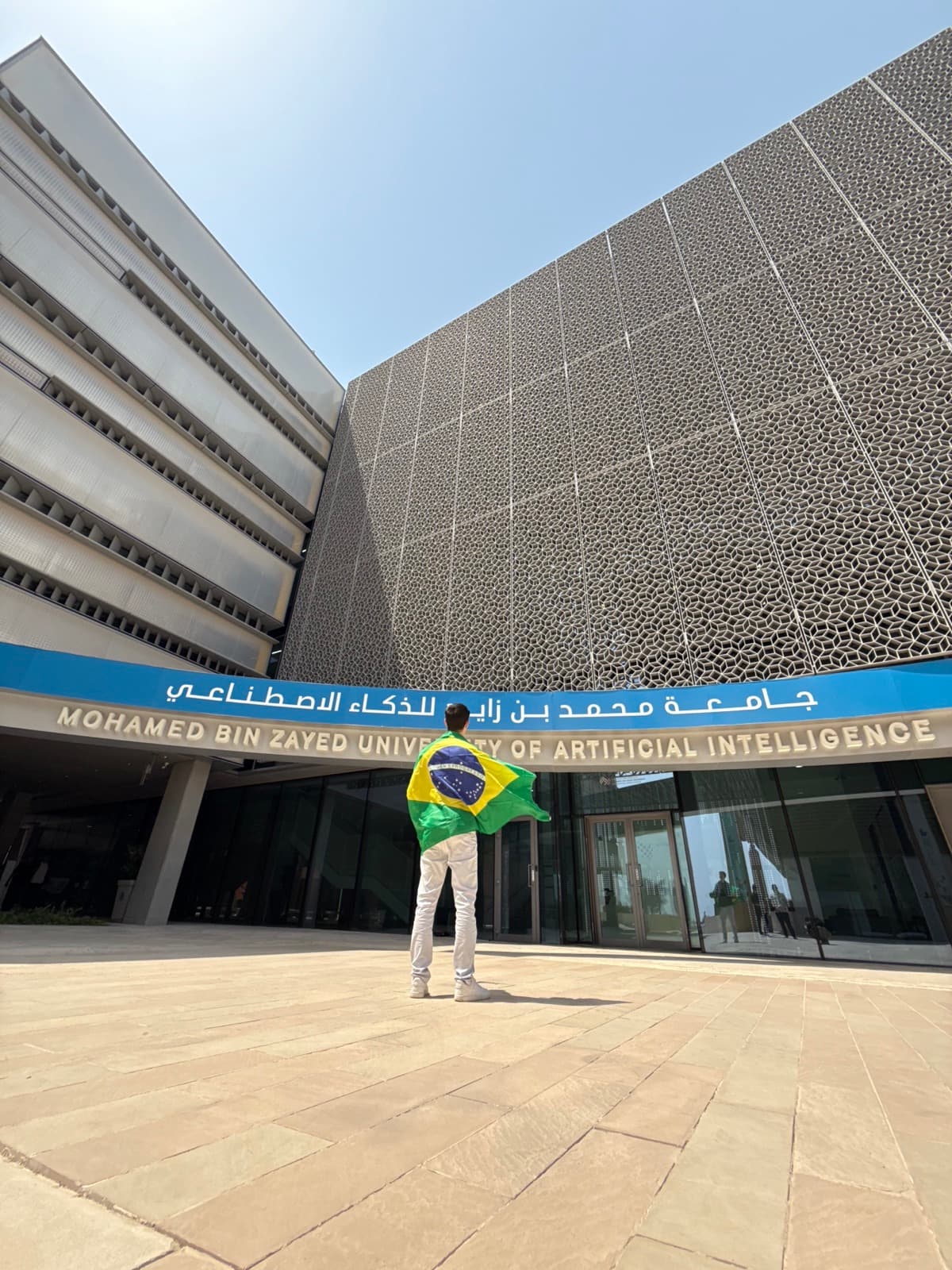 Me wearing a Brazilian flag at the main entrance of MBZUAI in Abu Dhabi
